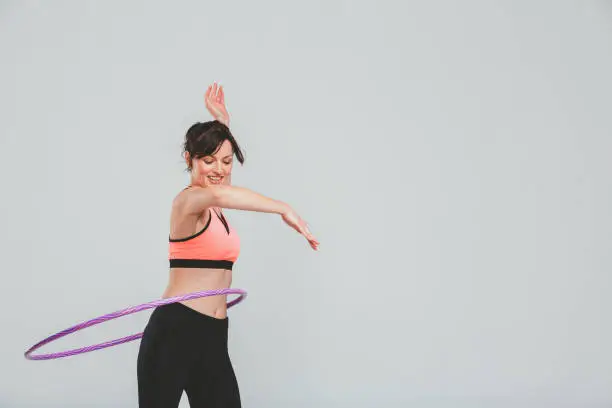Studio shot of a sporty young woman spinning a hula hoop around her hips against a grey background