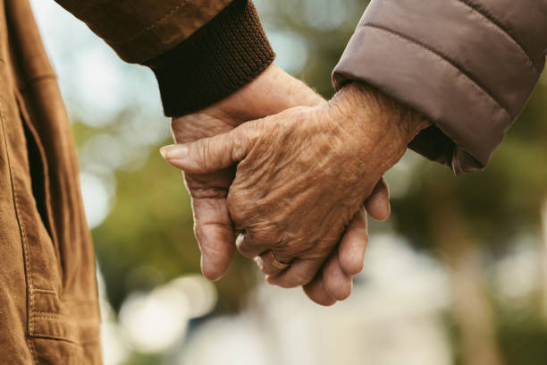 Elderly couple holding hands and walking Close up of elderly couple holding hands and walking outdoors. Rear view of man and woman holding hands of each other while walking outdoors. old hands stock pictures, royalty-free photos & images