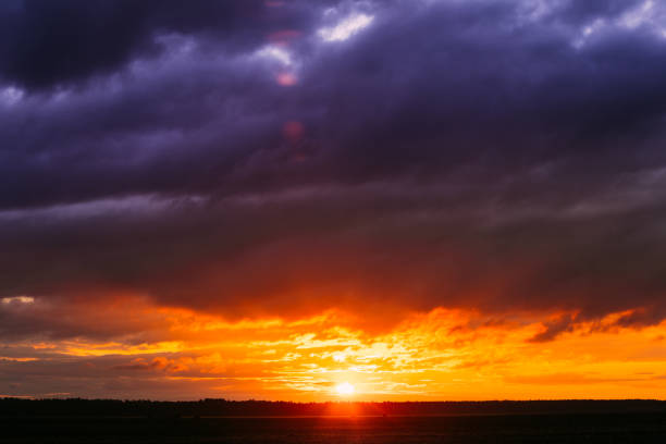 Sun At Sunset  Sunrise Sky. Bright Dramatic Sky With Clouds. Yellow, Orange, Blue And Magenta Colours. Dark Ground And Colorful Dawn Sky
