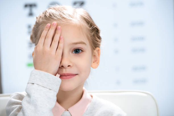 bambino che chiude l'occhio con il test degli occhi dietro - optometrie foto e immagini stock