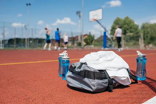 selective focus of sportive water bottles, bag and basketball players on playground