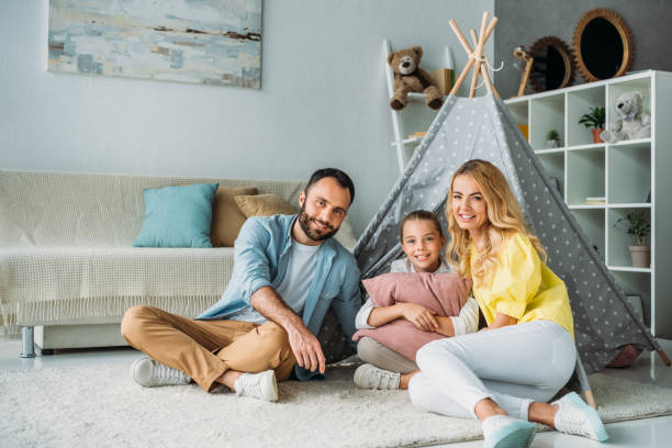 istock happy young family sitting on floor with teepee and looking at camera 1012530606