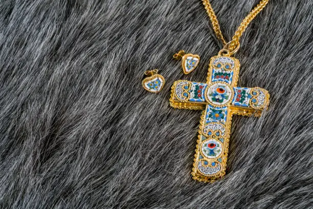Photo of Fashionable women's gold plated cross or crucifix necklace and earrings on grey fake fur