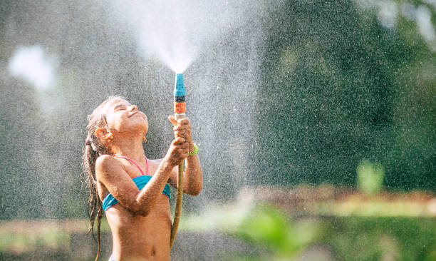 menina bonitinha serve-se da mangueira, faz uma chuva. prazer de dia quente de verão - mangueira de jardim - fotografias e filmes do acervo