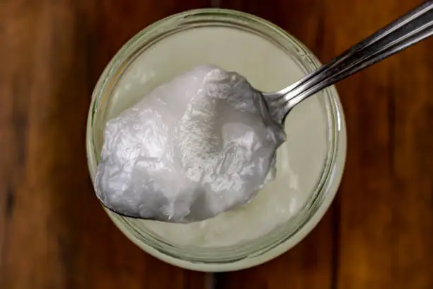 A spoonful of coconut oil set on a jar sitting on a wooden surface