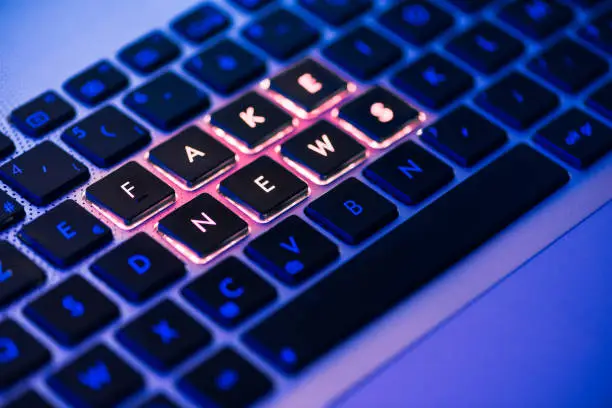 Fake news written in red on a backlit laptop keyboard close-up with selective focus in a blue ambiant light