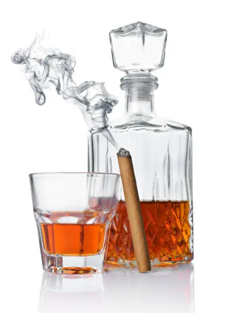 Strong alcoholic drink cognac in old fashion glass and crystal decanter with smoking cigar isolated on white background