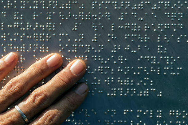 The fingers are touching the metal plate written in the Braille letters; helps the blind to recognize and communicate through the text. stock photo