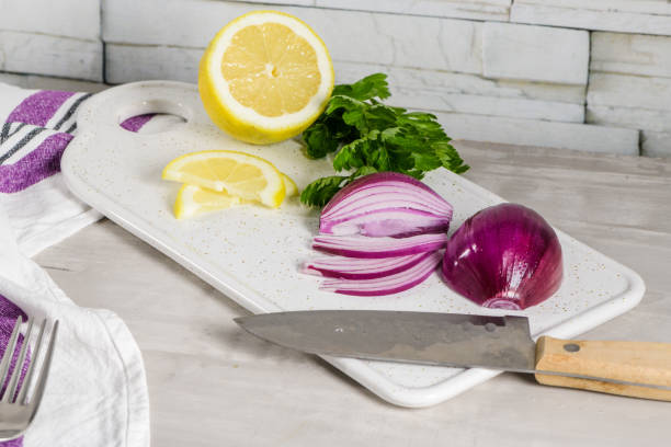 Sliced red onion, lemon and parsley leaves on white ceramic cutting board.