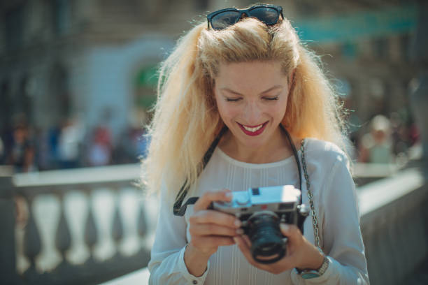 Beautiful blonde woman tourist in Ljubljana, Slovenia, standing downtown and taking pictures with camera.