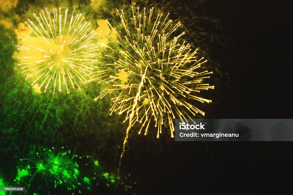 Fireworks background with beautiful yellow and green flowers projected on the night sky. Holiday relax time with a pyrotechnic show. Brightly fireworks on dark black color background. Festive event accompanied by holiday salves. Anniversary Stock Photo