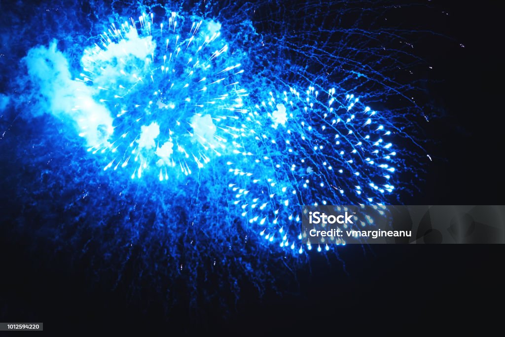 Amazing fireworks turquoise flowers on the night sky. Holiday relax time with a pyrotechnic show. Brightly fireworks on dark black color background. Festive event accompanied by holiday salves. Anniversary Stock Photo