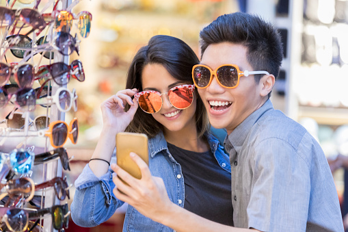 Tourists try on sunglasses in outdoor market in Singapore. They are taking a selfie while wearing trendy sunglasses.
