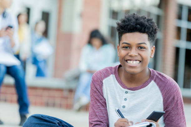 istock Studious teenage boy smiles for camera outside school 1012627758
