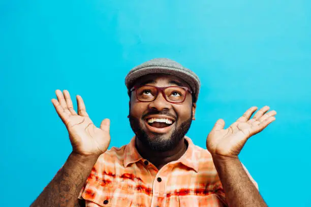 It's incredible! Portrait of a happy and excited man looking up with mouth open and both arms up, in front of a blue background
