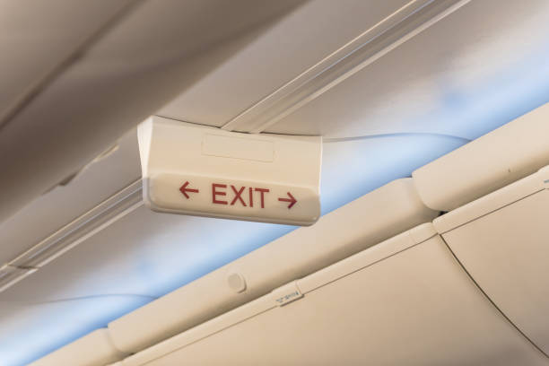 Emergency exit sign with red arrow on ceiling of airplane. Illuminated evacuation symbol underneath the overhead compartments. Shining signboard show escape of emergency, urgency, firer concept