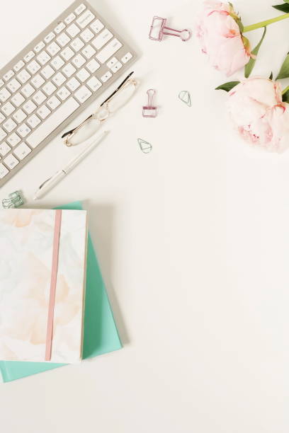 istock Flat lay women's office desk. Female workspace with flowers peonies,  accessories, notebook, glasses on white background. Top view feminine background.Copy space 1012702326