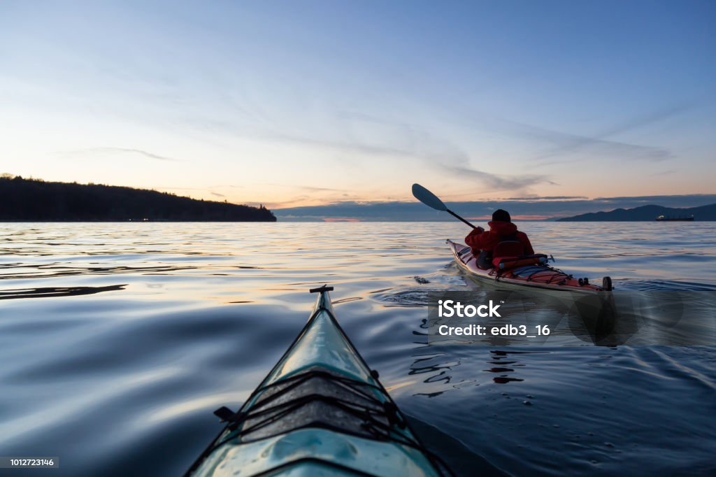 Sea Kayaking during sunset Adventure Man on a Sea Kayak is kayaking during a vibrant and colorful winter sunset. Taken in Vancouver, British Columbia, Canada. Adventure, Vacation Concept Kayaking Stock Photo