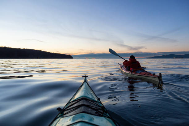 Sea Kayaking during sunset Adventure Man on a Sea Kayak is kayaking during a vibrant and colorful winter sunset. Taken in Vancouver, British Columbia, Canada. Adventure, Vacation Concept kayaking stock pictures, royalty-free photos & images