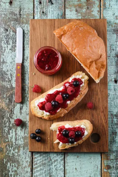 Homemade berry jam with fresh raspberries and currants on ciabatta toasts on wooden cutting boards top view