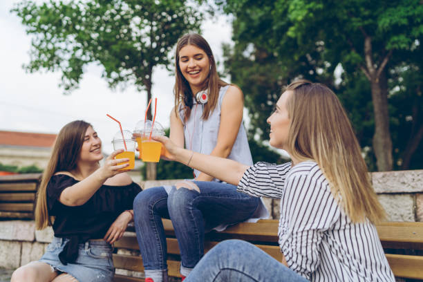 istock Three girlfriends toasting with orange juice on a bench 1012757444