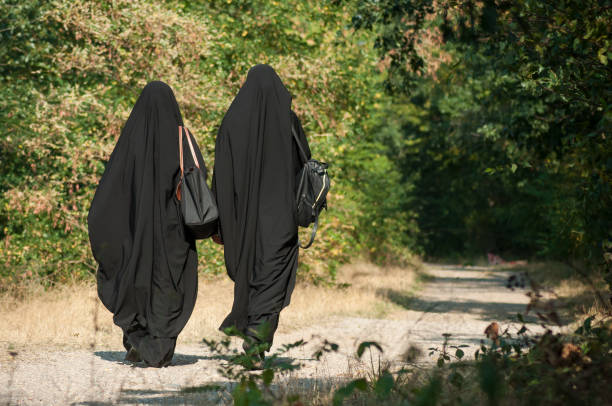 women walking in the forest with black niqab on back view stock photo