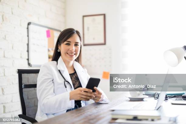 Happy Young Doctor With Phone At Office Stock Photo - Download Image Now - Doctor, Smart Phone, Healthcare And Medicine