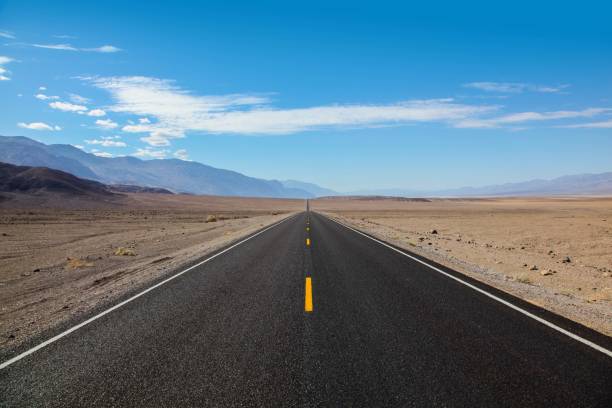 istock Endless and lonely blacktop road going into the mountain range entering Death Valley National Park 1012793540