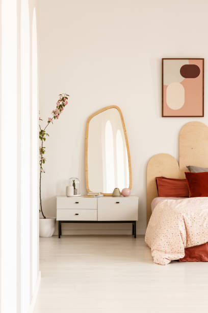 istock Mirror on white cabinet next to bed with headboard under poster in bright bedroom interior. Real photo 1012816574