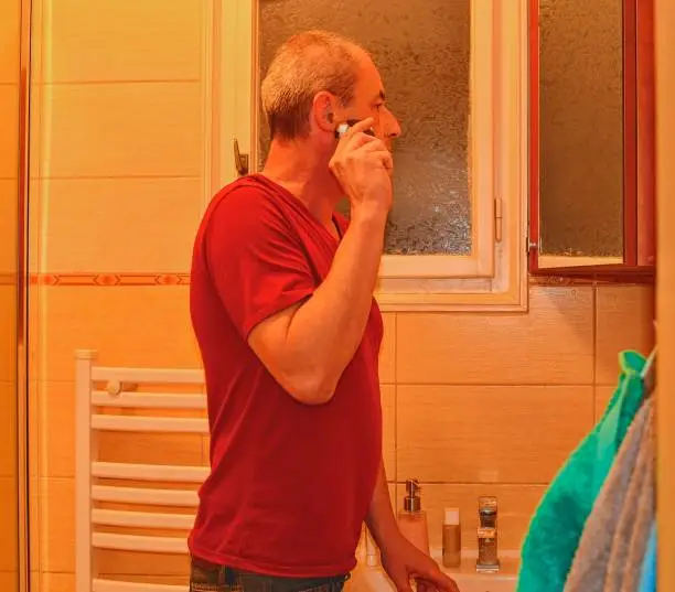 Middle aged man shaving in a bathroom, using electric razor. Senior concept. Mature man at home.