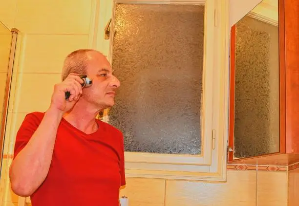 Middle aged man shaving in a bathroom, using electric razor. Senior concept. Mature man at home.