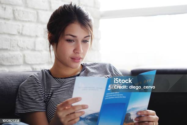 Woman Reading Travel Flye On Sofa At Home Stock Photo - Download Image Now - Brochure, Flyer - Leaflet, Reading