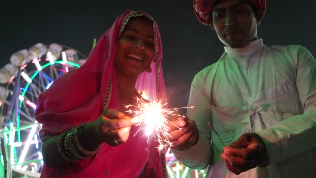 Indian couple in traditional dress with fire sparkle cracker at Diwali Mela festival in India