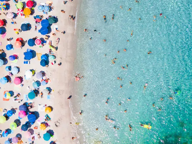 Photo of View from above, aerial view of an emerald and transparent Mediterranean sea with a white beach full of colored beach umbrellas and tourists who relax and swim. Costa Smeralda, Sardinia, Italy.