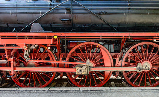 Beautiful well-maintained red-wheels of a vintage steam locomotive standing on rails at a station platform. Full-frame close-up image.