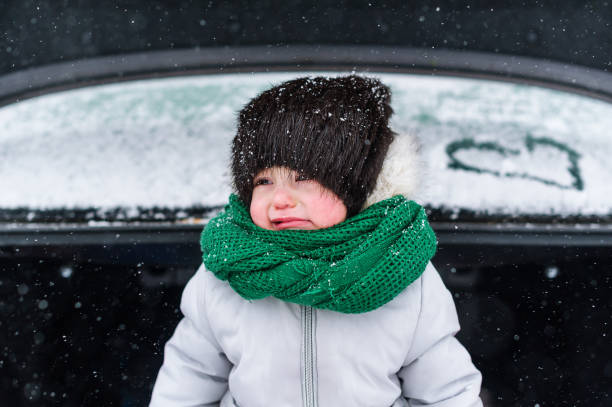 грустная маленькая девочка в теплой одежде, стоящая зимой в открытом багажнике автомобиля - winter clothing hat human eye стоковые фото и изображения