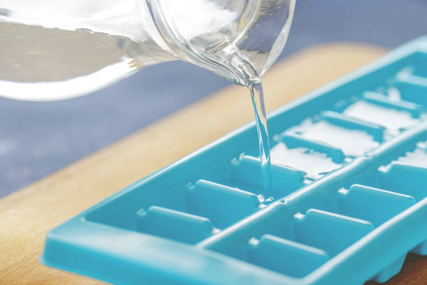 Pouring water into ice cube tray on the kitchen table. stock photo