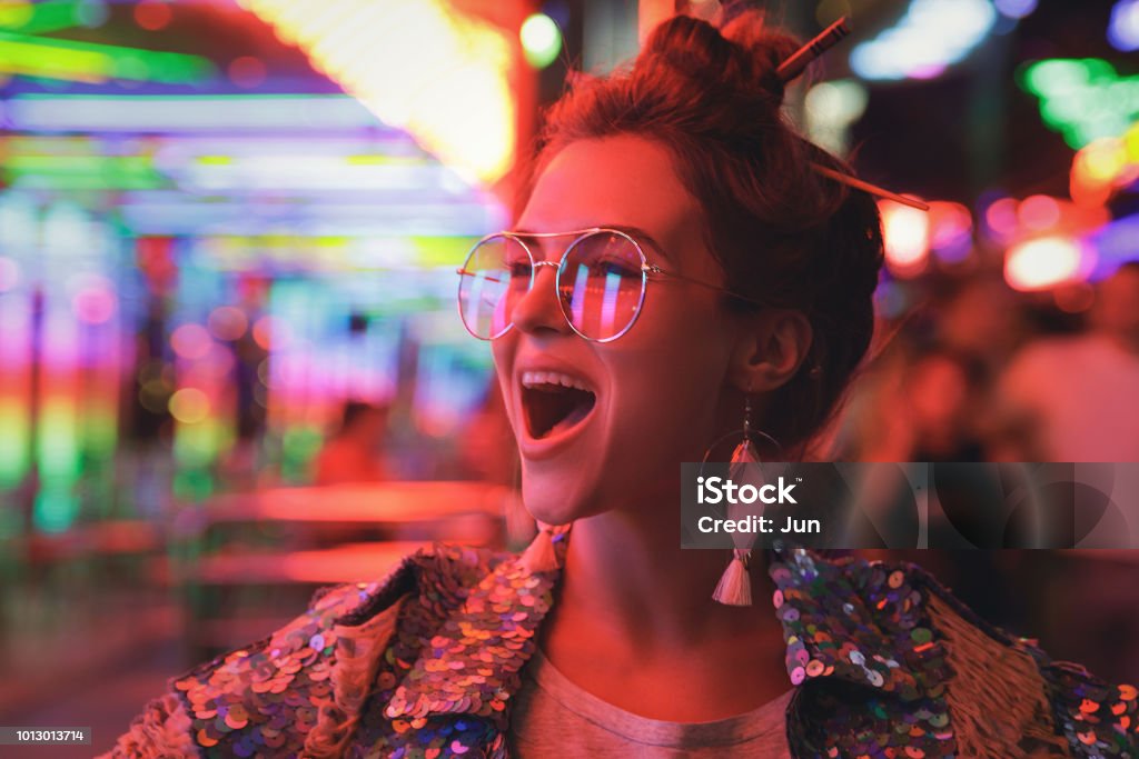 женщина в сверкающей куртке на городской улице с неоновыми огнями - Стоковые фото Вечеринка роялти-фри