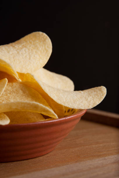 istock Many potato chips in round plate isolated on rustic wooden table and black background. Snack food. Vertical image. 1013039746