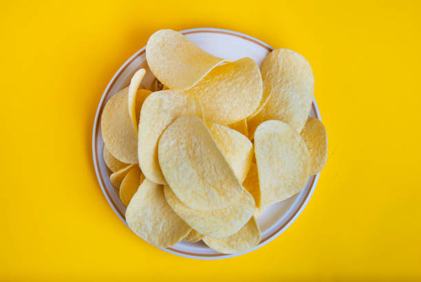 viele kartoffelchips in runde platte isoliert auf gelbem hintergrund. snack essen. ansicht von oben. - potato chip stock-fotos und bilder