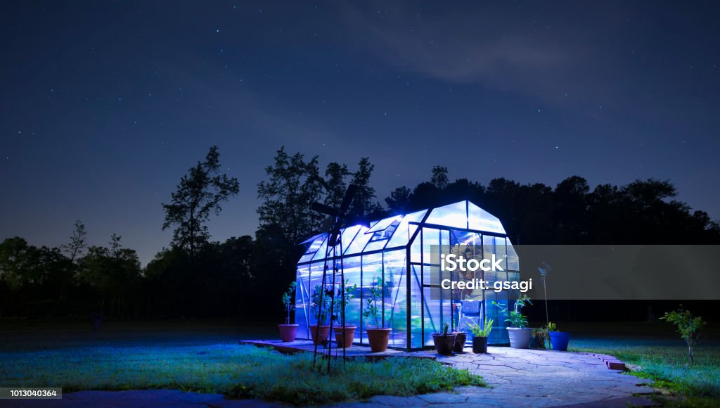 Lighted greenhouse after the sun has set Stars and clouds in the sky with a lighted greenhouse underneath Greenhouse Stock Photo