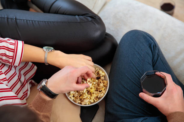 istock young couple sitting on couch eating popcorn close up 1013050198