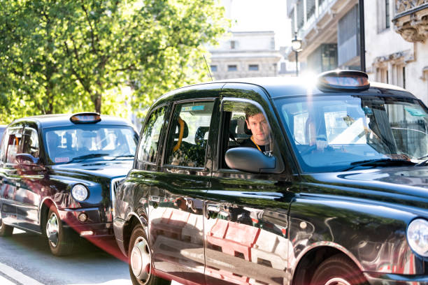 Closeup of expensive black taxi cab and driver on street road, young man behind wheel waiting in traffic London, UK - June 22, 2018: Closeup of expensive black taxi cab and driver on street road, young man behind wheel waiting in traffic taxi driver photos stock pictures, royalty-free photos & images