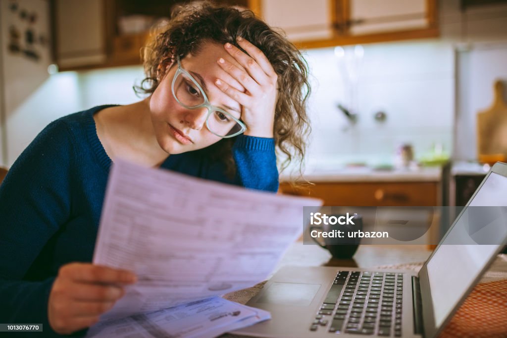 Woman going through bills, looking worried Young brunette curly female reading her bill papers, looking stressed Financial Bill Stock Photo