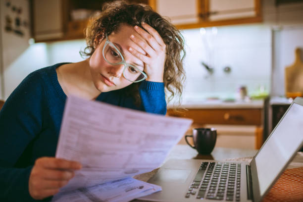 Woman going through bills, looking worried Young brunette curly female reading her bill papers, looking stressed salary stock pictures, royalty-free photos & images