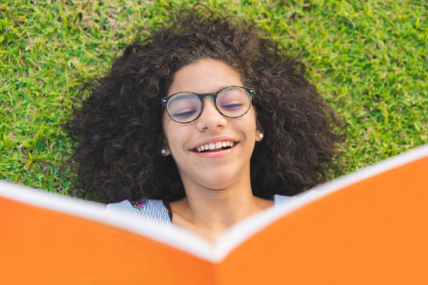 girl lying on the grass and reading a book - woman with glasses reading a book imagens e fotografias de stock