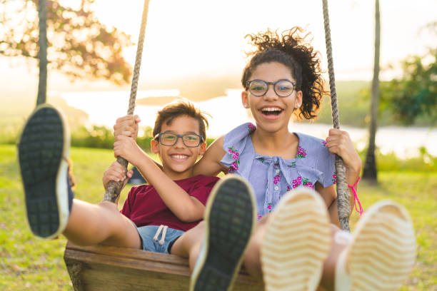 happy children swinging and smiling at golden sunset - swinging imagens e fotografias de stock