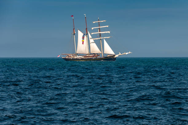 Gaff Schooner Sails Catch Light on Horizon Three-masted gaff schooner rig clearly defined as it sails left-to-right on blue ocean horizon. gaff sails stock pictures, royalty-free photos & images