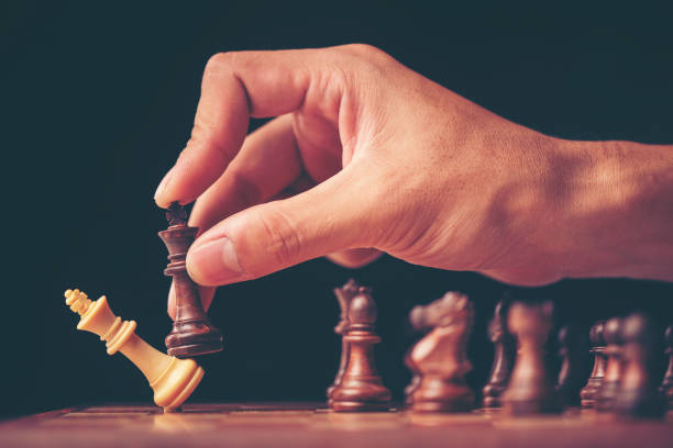 istock vintage style image of a businessman with clasped hands planning strategy with chess figures on an old wooden table. 1013168100