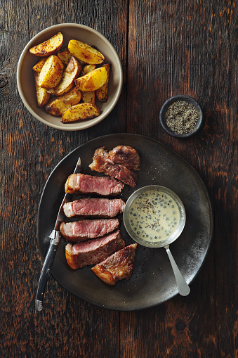 Steak with classic mustard and green peppercorns sauce on rustic wood background